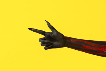 Black witch hand with claws pointing at something on yellow background. Halloween celebration