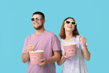 Happy young couple in 3D glasses with buckets of popcorn on blue background