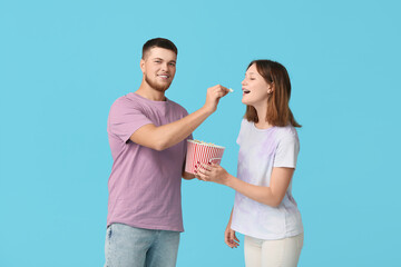 Happy young couple with bucket of popcorn on blue background