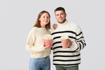 Happy young couple with buckets of popcorn on grey background