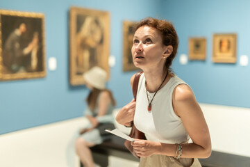 Adult woman with brochure looking around in art gallery of museum