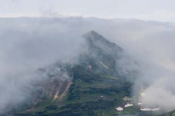 Summer mountain landscape. View of the mountain peaks. Low clouds. Travel, tourism and hiking on the Kamchatka Peninsula. Beautiful nature of Siberia and the Russian Far East. Kamchatka Krai, Russia.