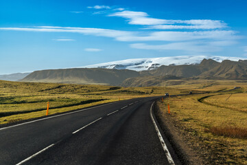 A winding road stretches towards towering mountains and glaciers in Iceland, with a dramatic sky overhead