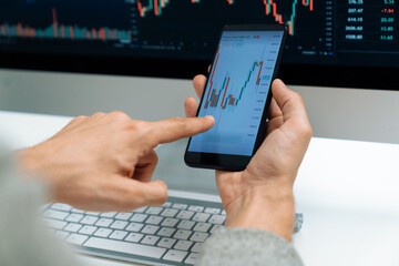 Smart stock investors pointing on screen with smartphone for market stock exchange along with laptop screen in highest dynamic investment rate, focusing data planning at modern workplace. Pecuniary.
