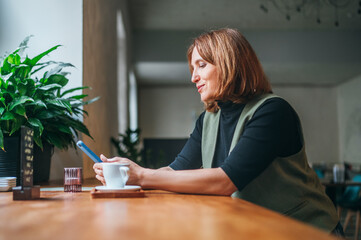 Portrait of brunette caucasian woman sitting at table in cozy cafe with little coffee cup and browsing internet using modern smartphone. Modern technologies, restaurant industry and business concept.