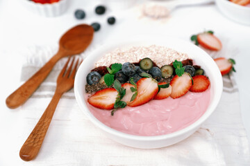 Presented by fruits putting yogurt toppings with strawberry, berry, oats, raisins and chia seed decorated by peppermint in white blow. Pink background. Set of healthy dairy product choice. Pecuniary.