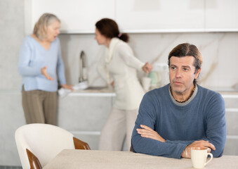 Distressed man is present during quarrel between his wife and elderly female mom. Mature woman and...