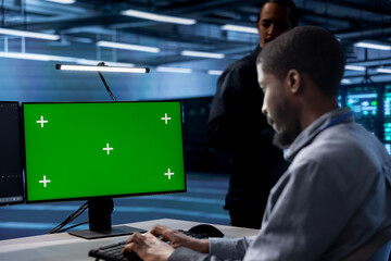 Focused software developer working on computer with green screen monitor in modern data center. IT professional doing IT infrastructure management on server racks in high tech environment
