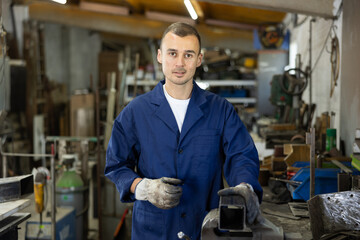 Male employee of workshop stands next to vise, resting from labors. Man takes break during...