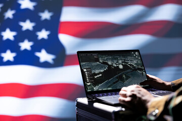 US Air Force officer isolated over USA flag monitoring zone of interest using radar. Close up shot of United States military soldier engaged in surveillance mission using laptop, looking at world map