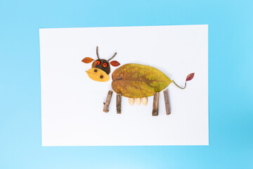 Natural materials art piece resembling animal cow. Crafted from leaves, twigs, seeds. Brownish yellow leaf body, yellow leaf head twig legs,