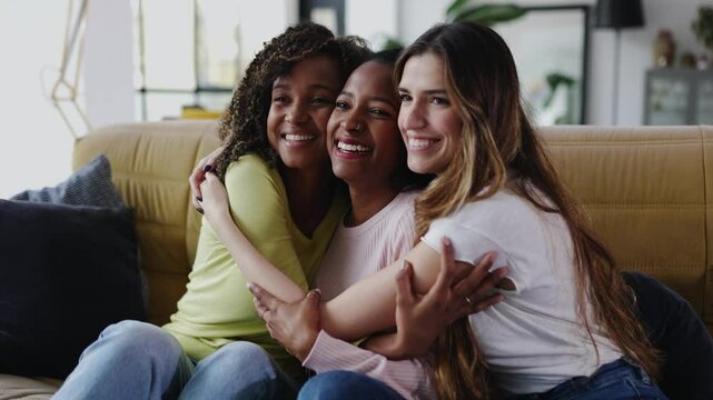 United multiracial female friends sitting together on sofa. Happy multiracial women embracing each other sitting on couch. Female friendship and love concept.