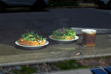 Arugula Toast and Cold Brew Coffee on Café Table Viewed from Street