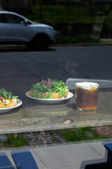 Café Table with Arugula Salad on Toast and Cold Brew Coffee Viewed Through Window