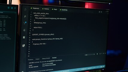 Extreme close up of software interface on PC screens showing lines of code running in empty criminals den. Hacking malware programming script on displays in underground base, handheld camera shot