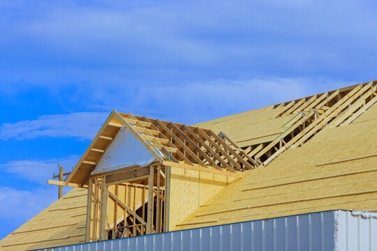 Installation of plywood on wooden roofing trusses at roof of house that is being constructed