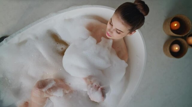 Peaceful lady relaxing bubbles bath touching gentle skin top view. Woman lying