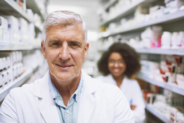 Fototapeta premium Portrait, confident and mature man in pharmacy, smile and wellness of medicine, store and happy with product. Healthcare, lab coat and pharmacist with antibiotics, shelf and packaging of pills