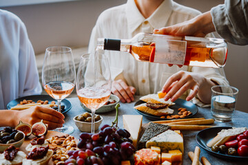 Pouring rose wine with classic snacks of cheese, bread and olives. Party or anniversary celebration.