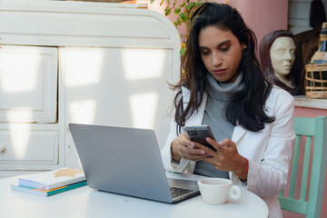 Woman at home working with phone and laptop sending messages to clients