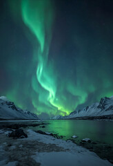 Naklejka premium Northern Lights Aurora Borealis flashes in dramatic night sky over snowcapped mountain range and frozen mount lake at polar nighttime. With no people serene snowy winter landscape 3D illustration.