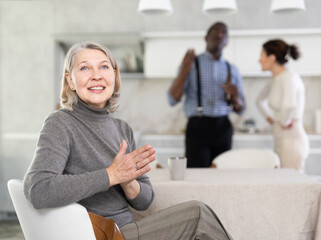 Elderly woman smiling during family quarrel between couple of adult man and woman in kitchen