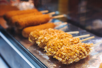 Korean Street Food - corn dogs, variety of different traditional food selection in Seoul, South Korea, night street market with local vendor stalls cooking tasty dishes, Republic of Korea cuisine
