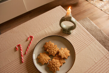 Merry Christmas! Gingerbread cookies lie in a plate on the table, there is a candle and lollipops. The background is a beautiful cozy home interior. Time for family