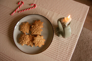Merry Christmas! Hand holding gingerbread man cookie with icing on background of cookies in plate on table against christmas tree golden lights. Atmospheric Christmas holidays, family time