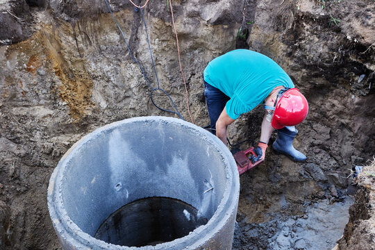 Construction worker is chiseling big hole in concrete ring with rotary hammer.
