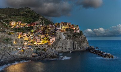 Twilight Coastal Village (Manarola - Italy).
The village lights flicker as the sun sets, casting a...