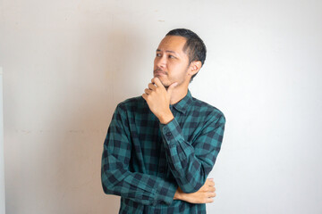 Young Adult bearded Asian man wearing green flannel shirt showing thinking gesture. Hip on chin