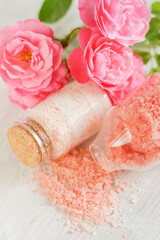  salt with rose fragrance. Cosmetic product with rose extract.Set of spa bath salts in glass jars and pink roses flowers on shabby white background.Aromatherapy and cosmetic