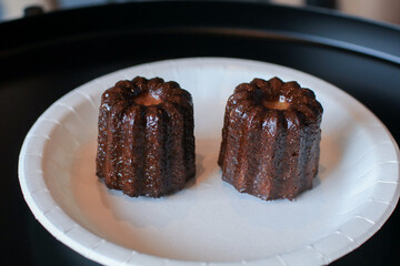 Hand pick up Homemade Canelés de Bordeaux pastry with rum and vanilla in white plate. Caramelized crust specialty. Traditional French sweet dessert