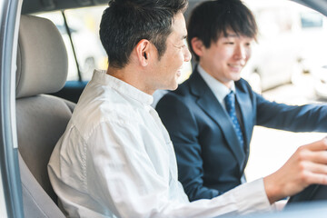 ショールームで自動車の車内で営業マンの説明を受ける顧客の男性
