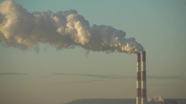 The two chimneys of the power plant give off white puffs of smoke, pollution of the atmosphere. Global warming Man's Carbon Footprint. Electricity production with fossil fuel concept. Polluting