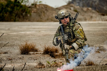 A group of military men in combat gear patrol in the middle of a desert and tropical jungle. Soldiers in full combat gear in dry weather conditions assemble and march on a mission.