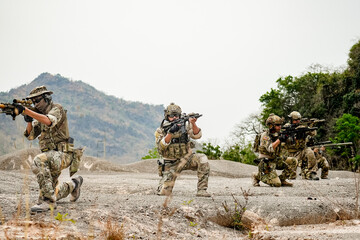 Fototapeta premium A group of military men in combat gear patrol in the middle of a desert and tropical jungle. Soldiers in full combat gear in dry weather conditions assemble and march on a mission.