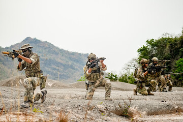 A group of military men in combat gear patrol in the middle of a desert and tropical jungle....