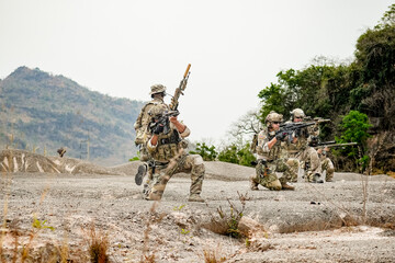 A group of military men in combat gear patrol in the middle of a desert and tropical jungle. Soldiers in full combat gear in dry weather conditions assemble and march on a mission.