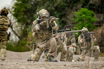 A group of military men in combat gear patrol in the middle of a desert and tropical jungle....