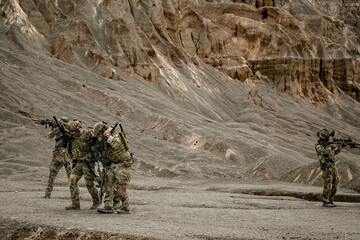 A group of military men in combat gear patrol in the middle of a desert and tropical jungle....