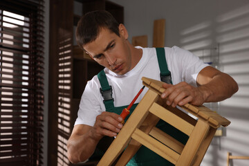 Obraz premium Man repairing wooden stool with screwdriver indoors