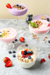 Different tasty yogurts with fresh berries and granola in glass dishware on gray textured table