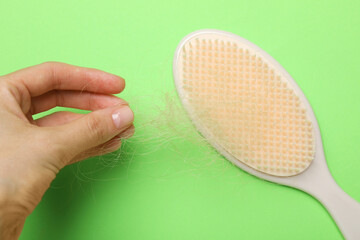 Woman taking her lost hair from brush on light green background, top view. Alopecia problem