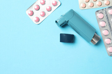 Asthma inhaler and pills on light blue background, flat lay. Space for text