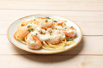 Tasty pasta with shrimps, creamy sauce and cheese on light wooden table, closeup