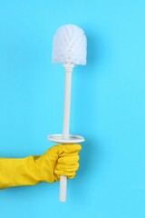 Woman holding white toilet brush on light blue background, closeup. Cleaning tool