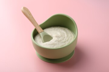 Delicious baby food in bowl and spoon on pink background