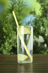 Glass of soda water with lime on wooden table against blurred background